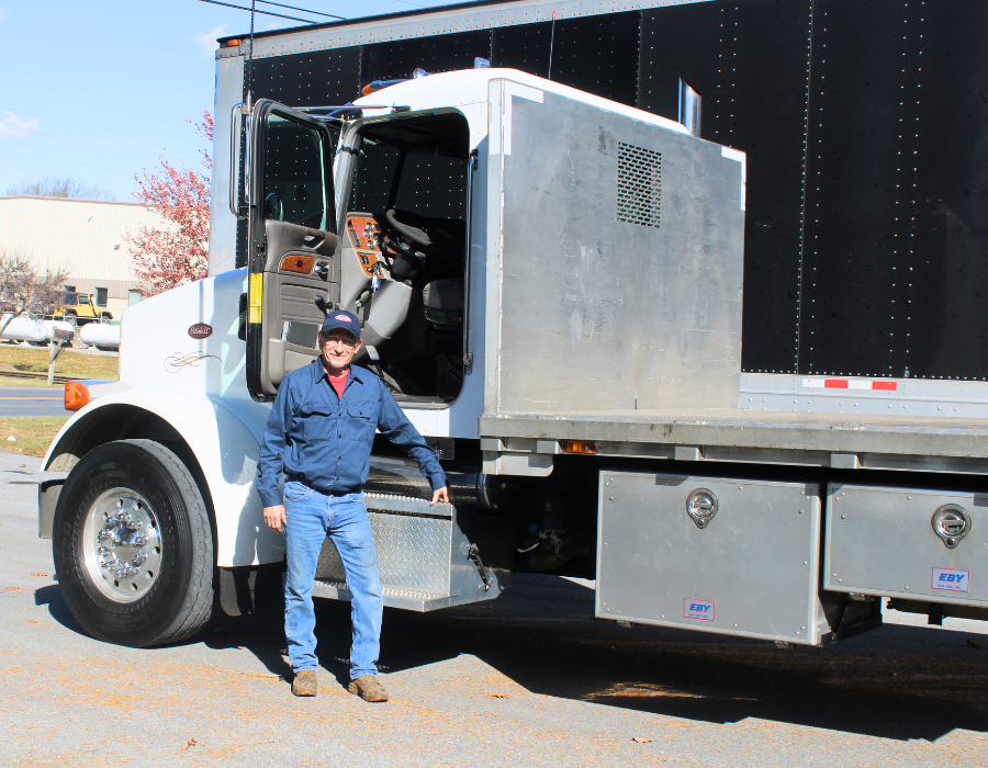 Male employee standing in front of a flatbed truck